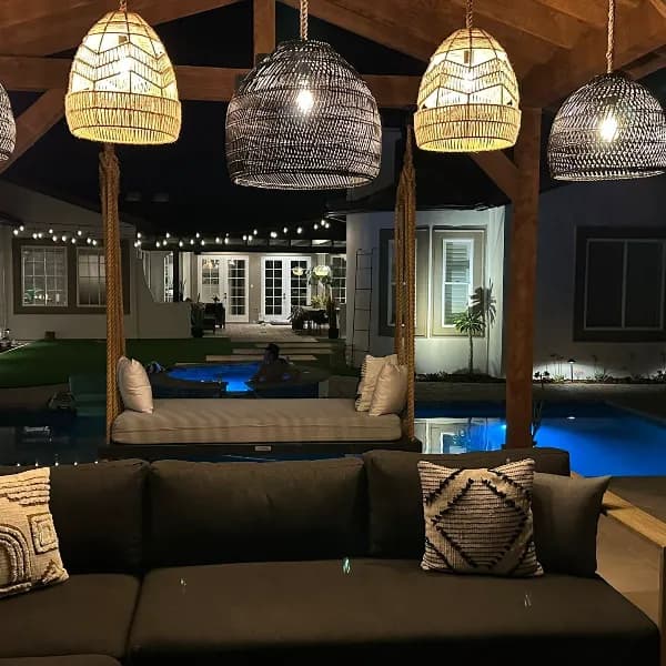 Luxury backyard pergola with hanging daybed swing and illuminated pool featuring custom wicker pendant lights and rope-wrapped wood posts in San Diego