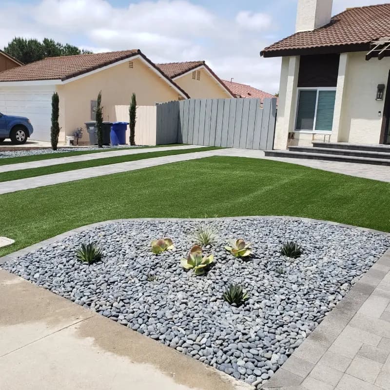 Modern front yard featuring geometric artificial turf layout with decorative white river rock garden bed and drought-tolerant succulents