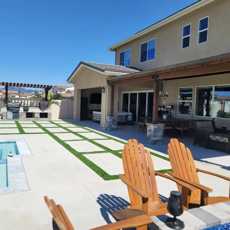 Contemporary pool deck featuring oversized concrete pavers alternating with synthetic turf strips in geometric pattern, orange Adirondack chairs, and built-in outdoor kitchen